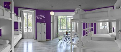 A modern hotel room with bunk beds, a purple accent wall, and a large window offering a view of the outdoors.