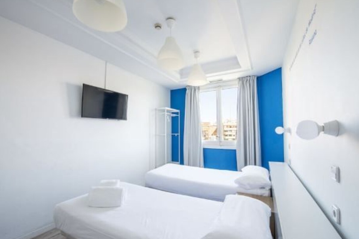 A hotel room with two beds, a TV, a window with curtains, and a city view.