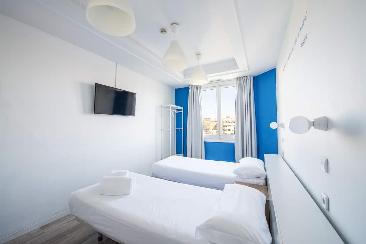 Une chambre d’hôtel avec deux lits simples, un téléviseur à écran plat fixé au mur, une fenêtre avec des rideaux et une vue sur le paysage urbain.