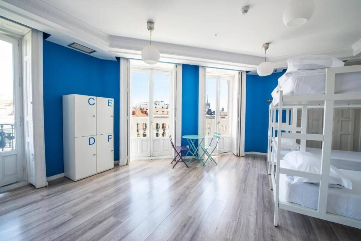 Une chambre avec des lits superposés, une armoire ornée de lettres de l’alphabet, une petite table avec des chaises et de grandes fenêtres donnant sur des immeubles.
