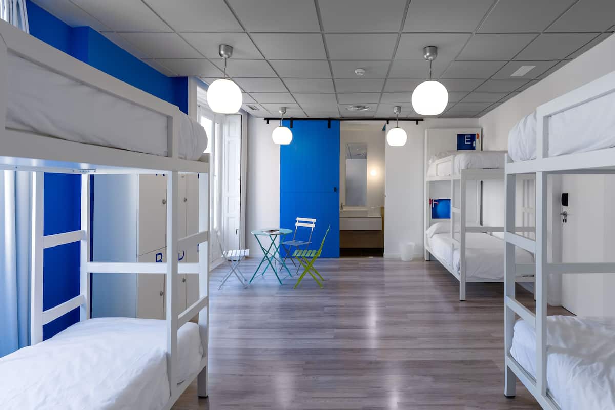 Une chambre de dortoir avec des lits superposés, une petite table avec des chaises et un mur bleu.