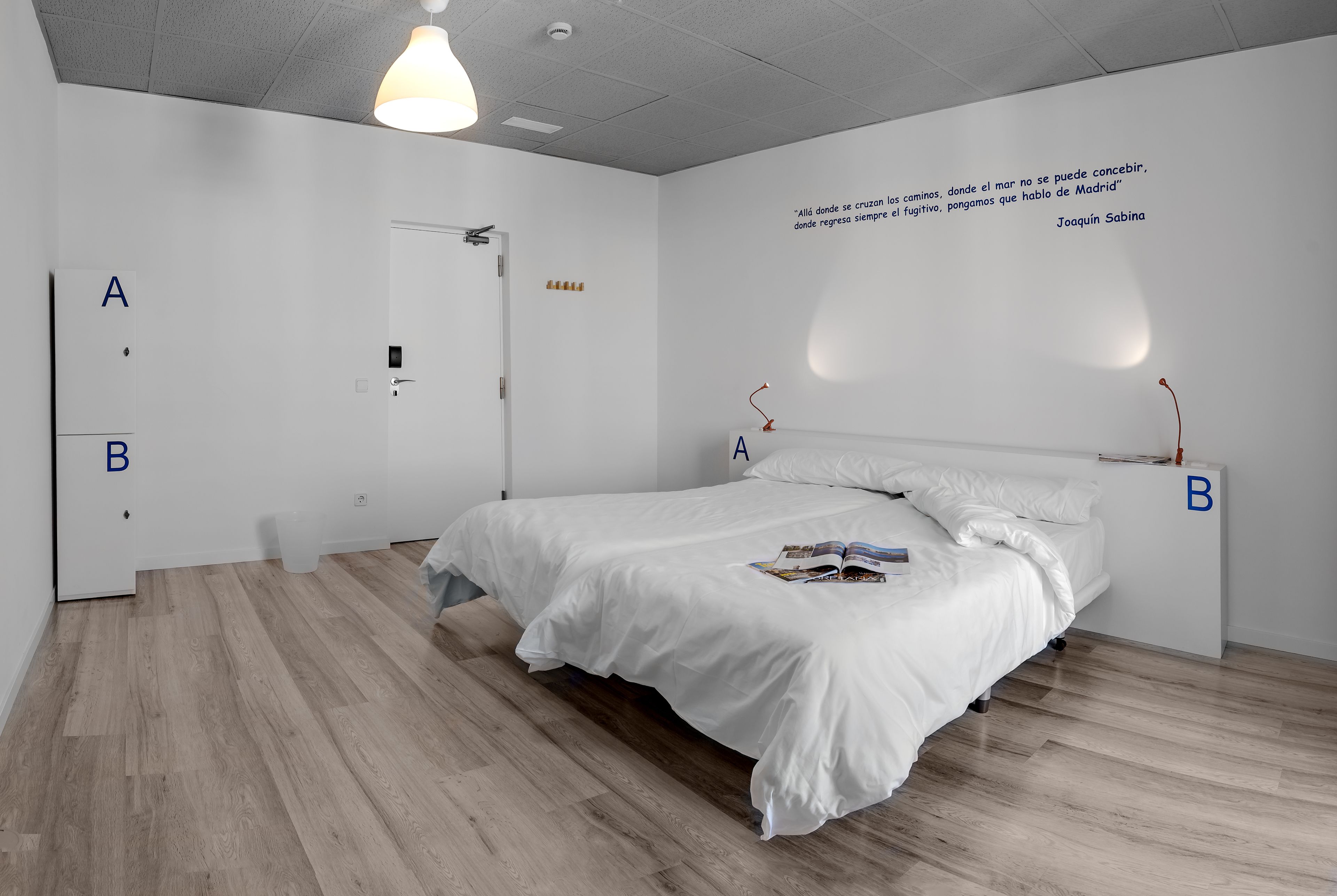 A minimalist bedroom with a large bed, a wardrobe, and a wall with a quote.