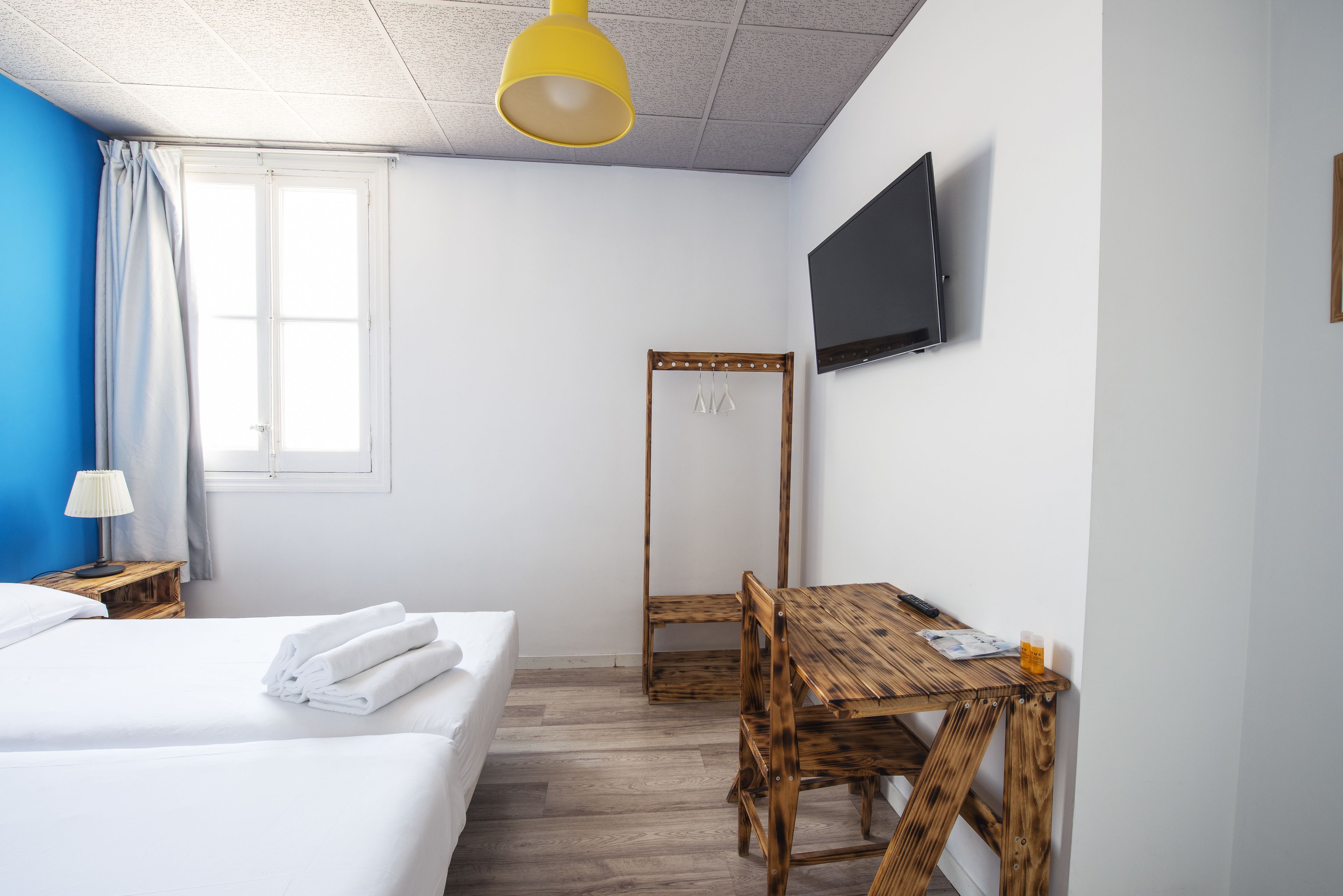 Una habitación de hotel con cama, una mesa de madera, televisor y ventana con cortinas.