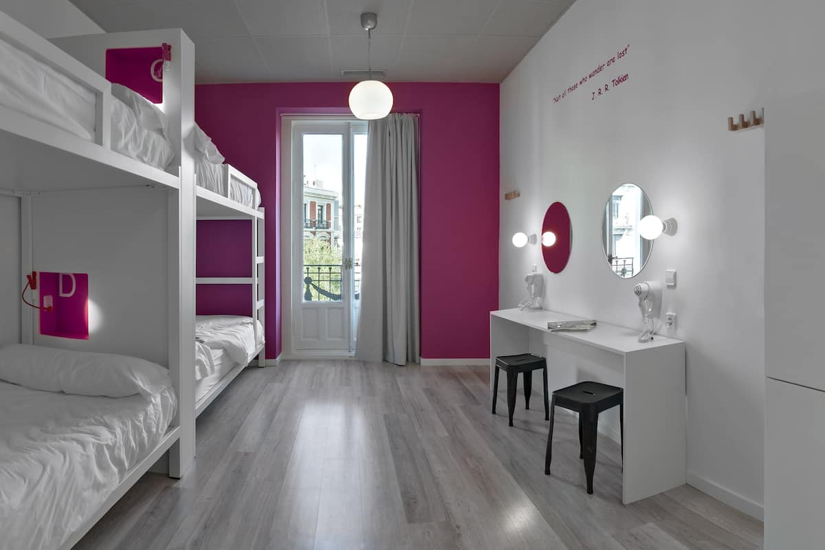 Une chambre avec des lits superposés, une coiffeuse avec un miroir et des lampes, et une porte donnant sur un balcon.