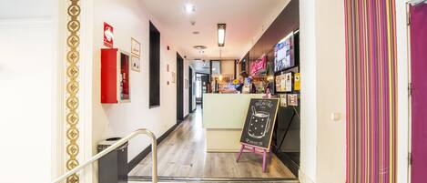 A hotel hallway with a reception desk, a neon sign, and a chalkboard sign.