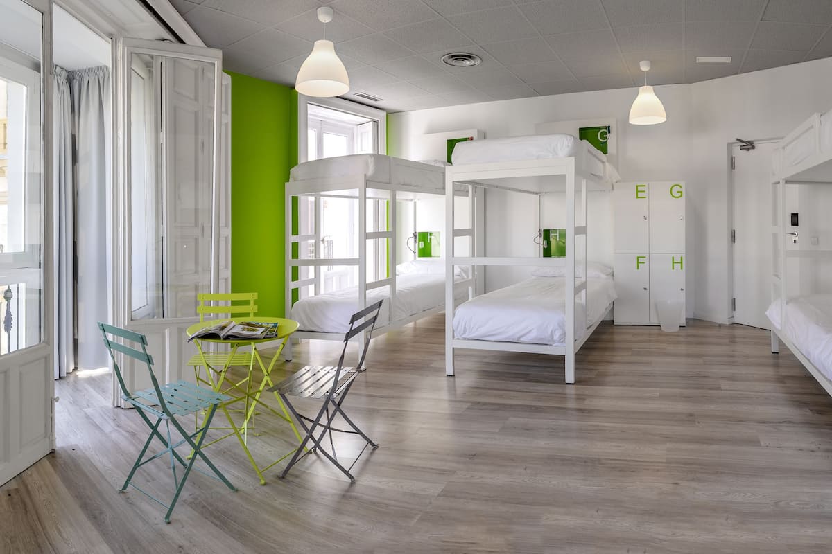 Une chambre avec des lits superposés, un bureau avec des chaises et une fenêtre avec des rideaux.