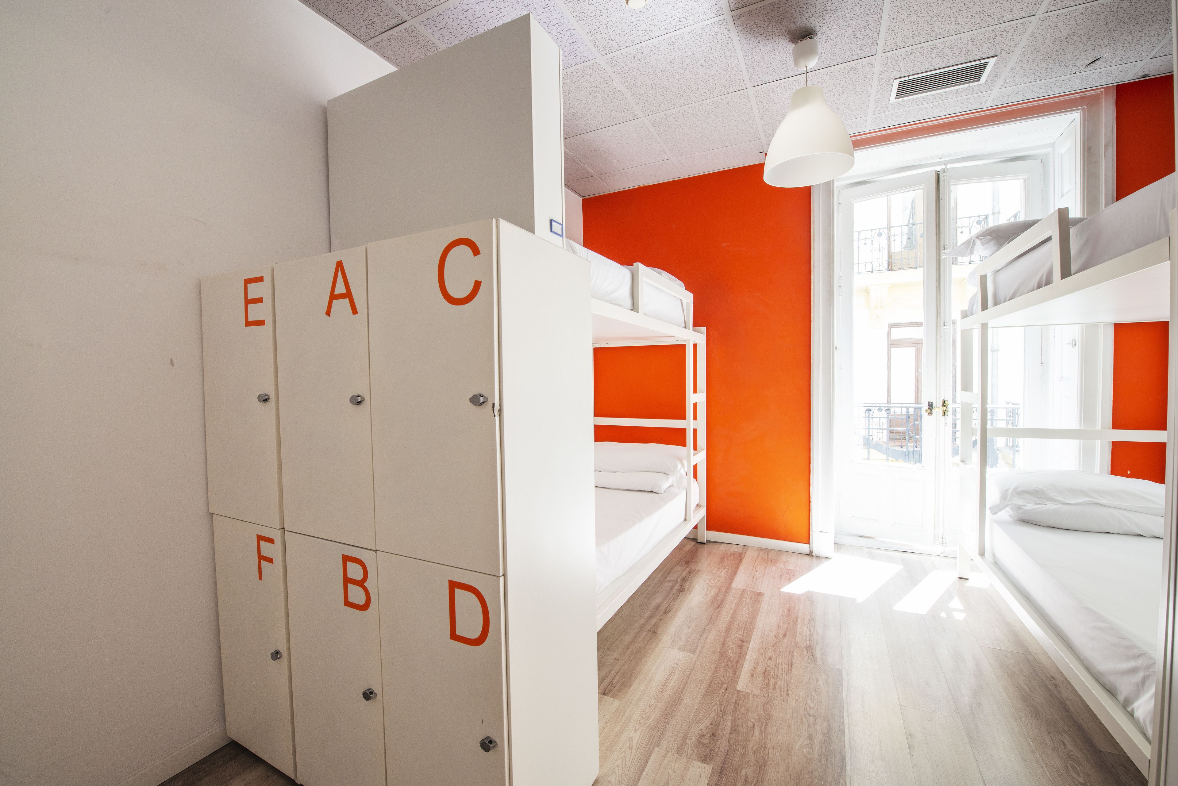 Un dormitorio con literas, un armario con etiquetas alfabéticas y una pared de color naranja brillante.