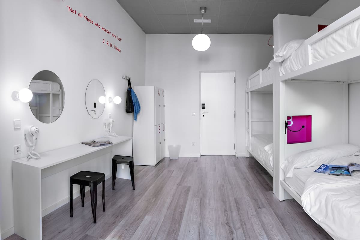 Une chambre moderne et minimaliste, dotée de lits superposés, d’une coiffeuse avec des miroirs, d’un sèche-cheveux et d’une porte avec une poignée.