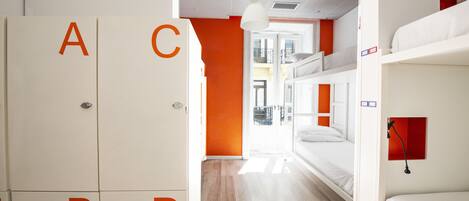 A dormitory room with bunk beds, a wardrobe with alphabet labels, and an orange accent wall.
