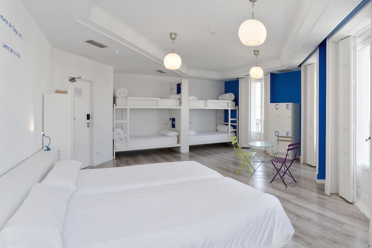 Une chambre d’hôtel avec un grand lit, des lits superposés, un bureau et une chaise.