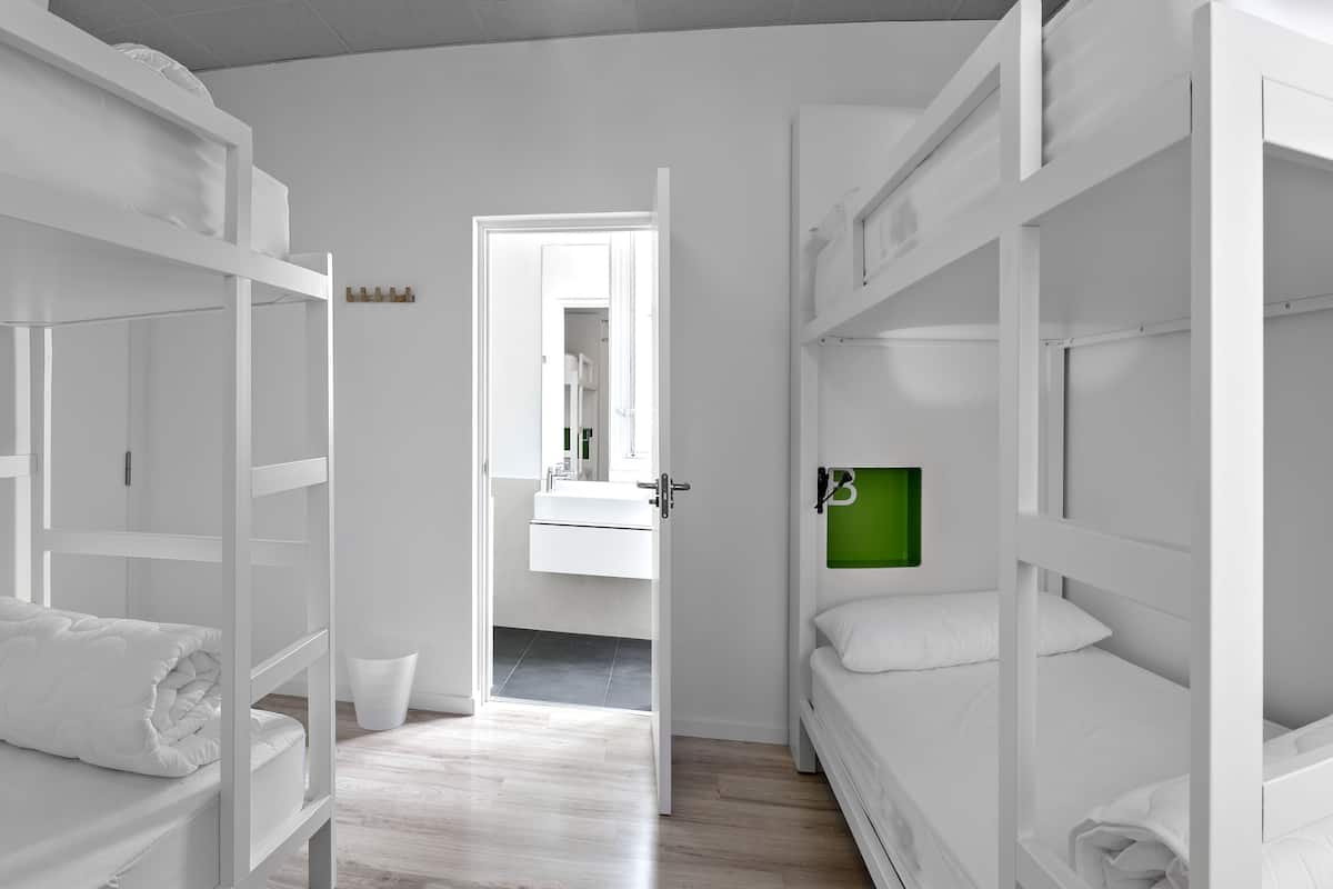 Une chambre avec des lits superposés, une petite salle de bain avec un miroir et un objet encadré de vert accroché au mur.