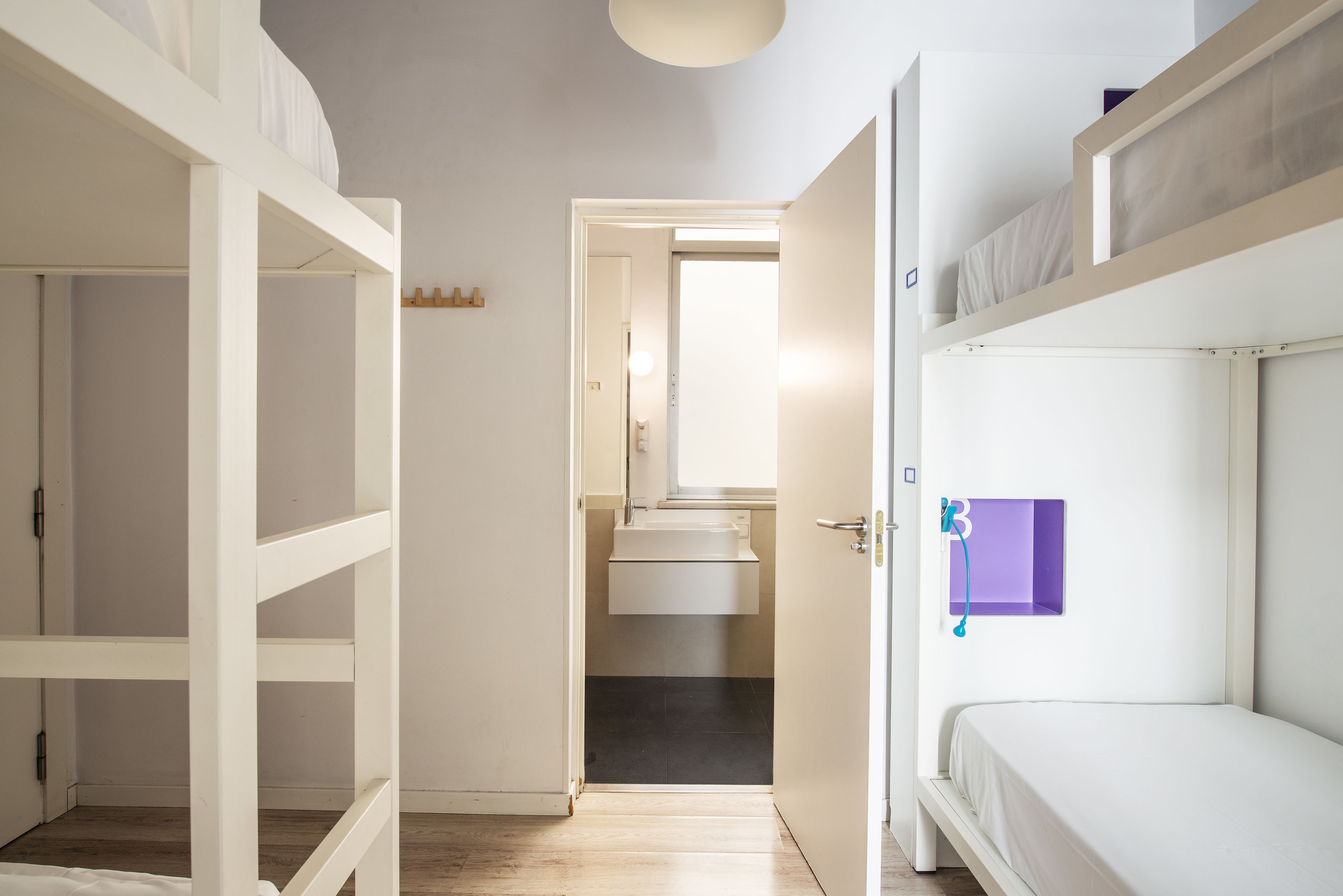 A room with bunk beds, a small bathroom with a sink, and a door leading to another room.