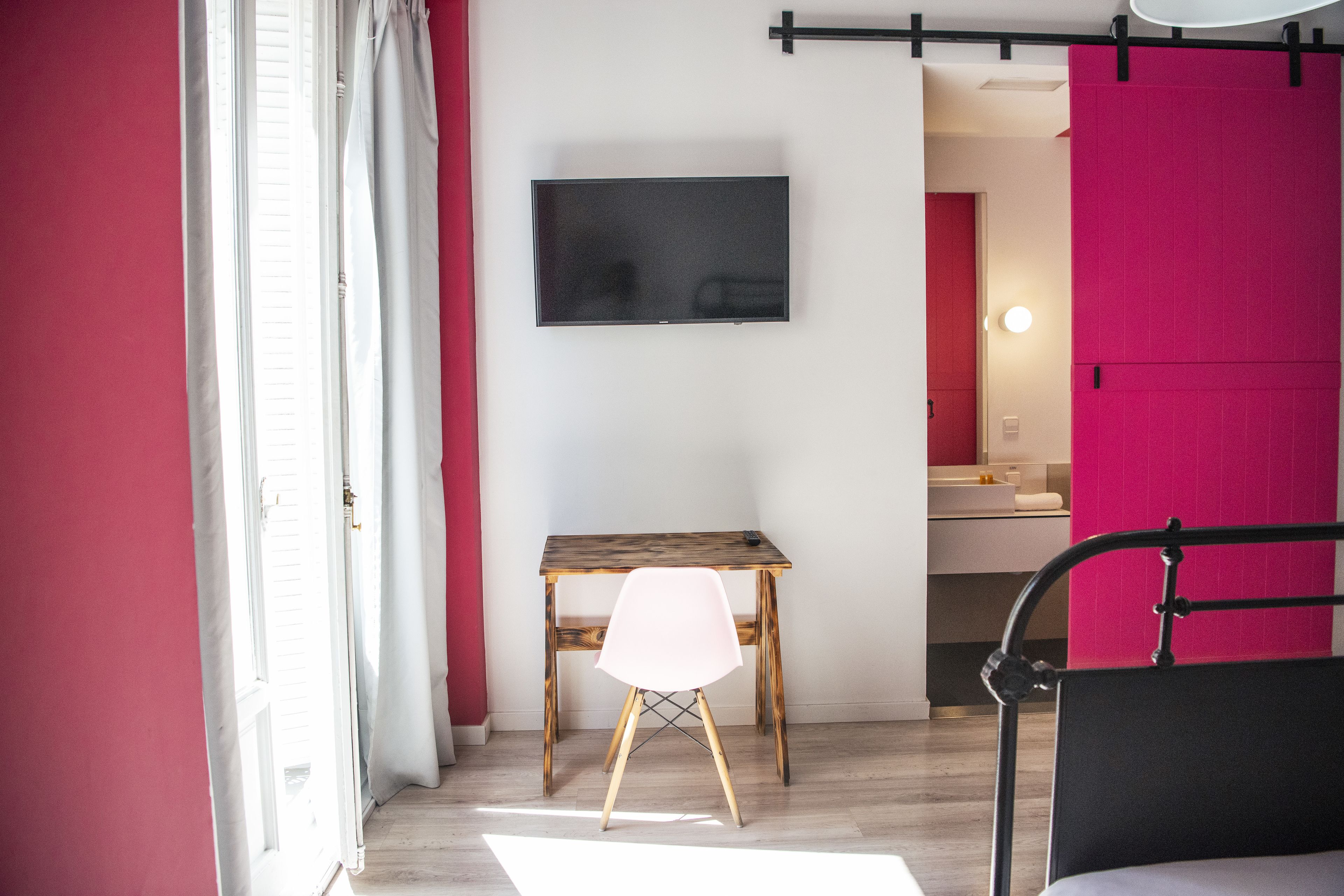 Una habitación con un escritorio de madera, una silla blanca, una cama y un televisor montado en la pared.