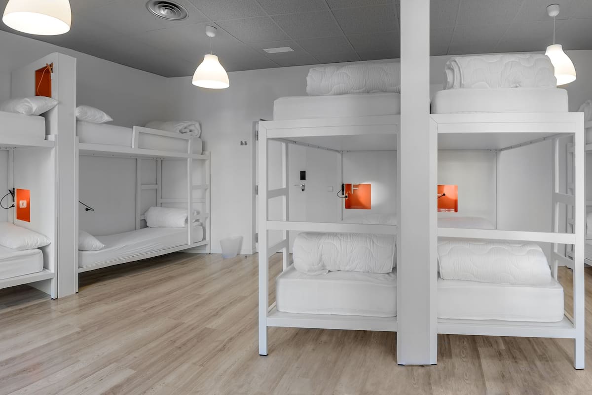 Une chambre de dortoir avec des lits superposés, des murs blancs et un plancher en bois.