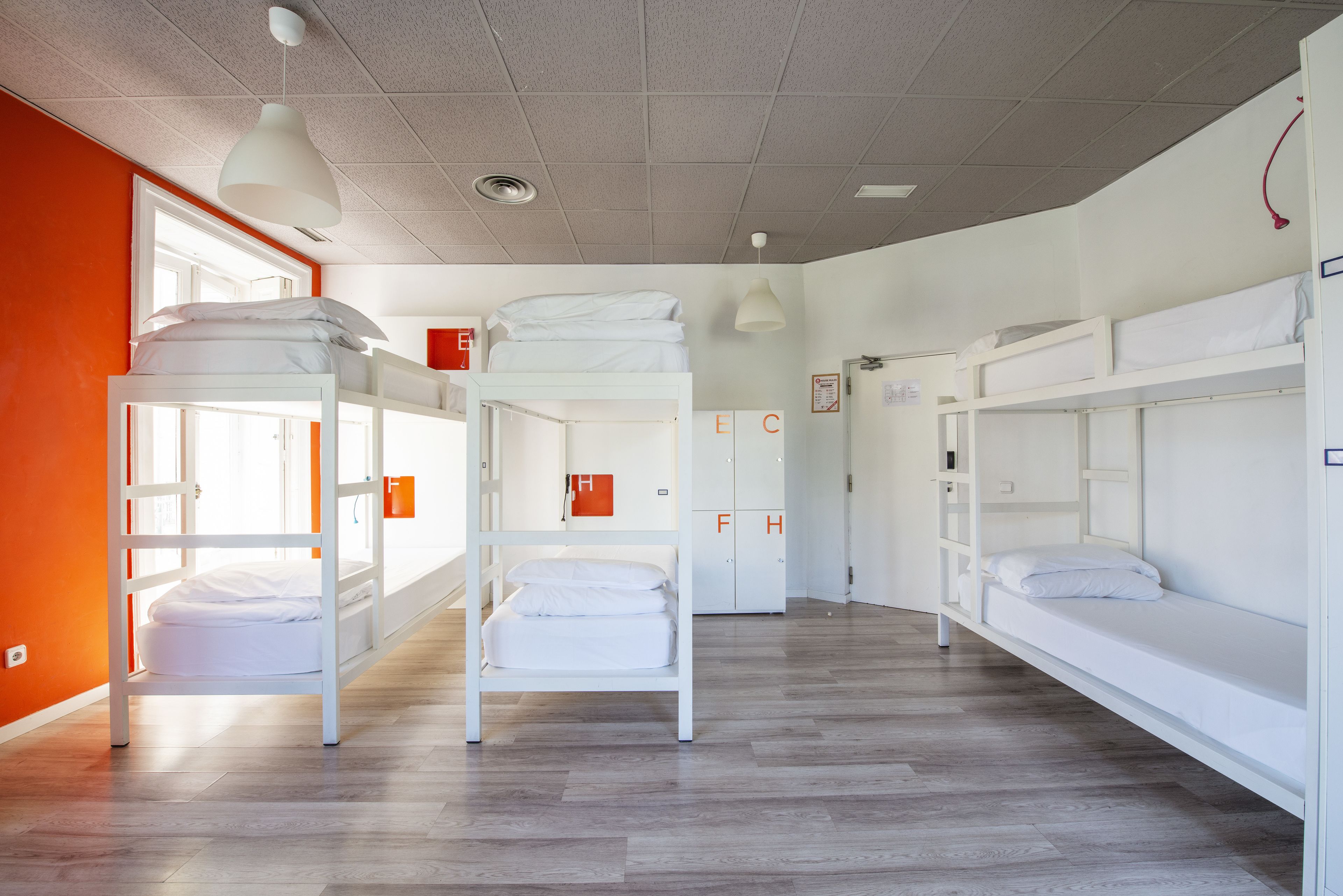 A dormitory room with bunk beds, a window, and a door with emergency exit signs.
