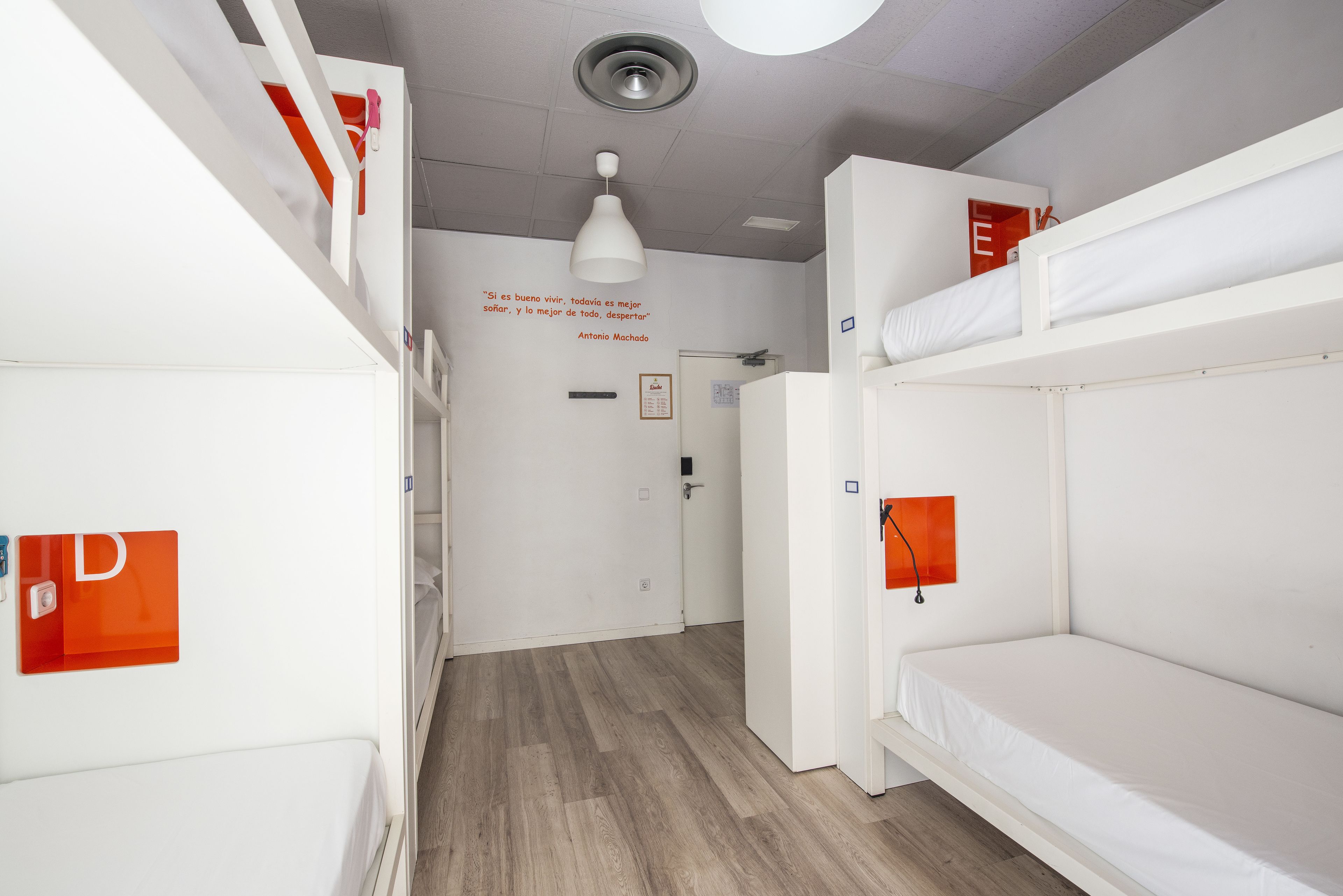 Een slaapzaal met stapelbedden, een wit plafond en een houten vloer.
