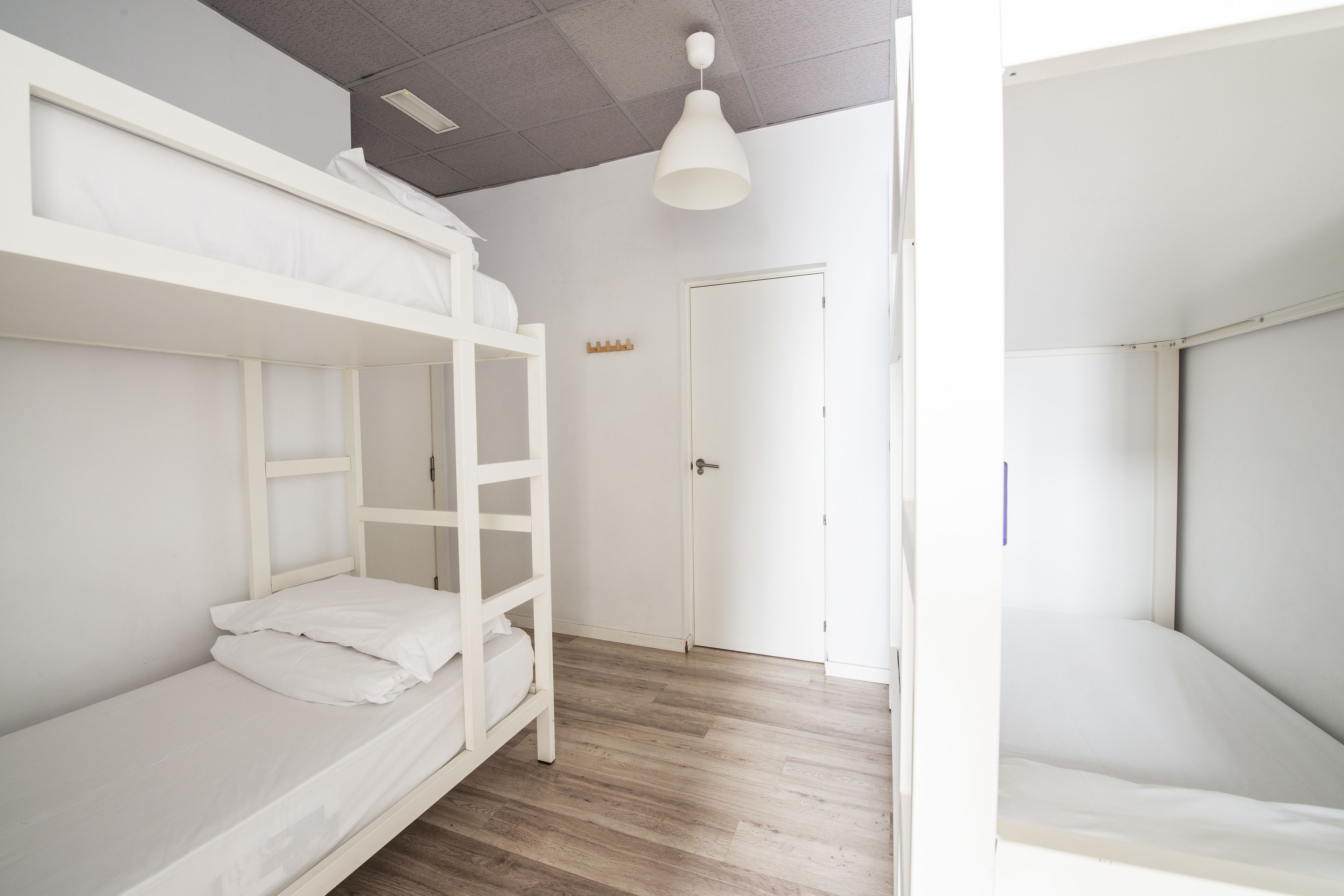 Un dormitorio con literas, suelo de madera, una puerta blanca y una lámpara en el techo.