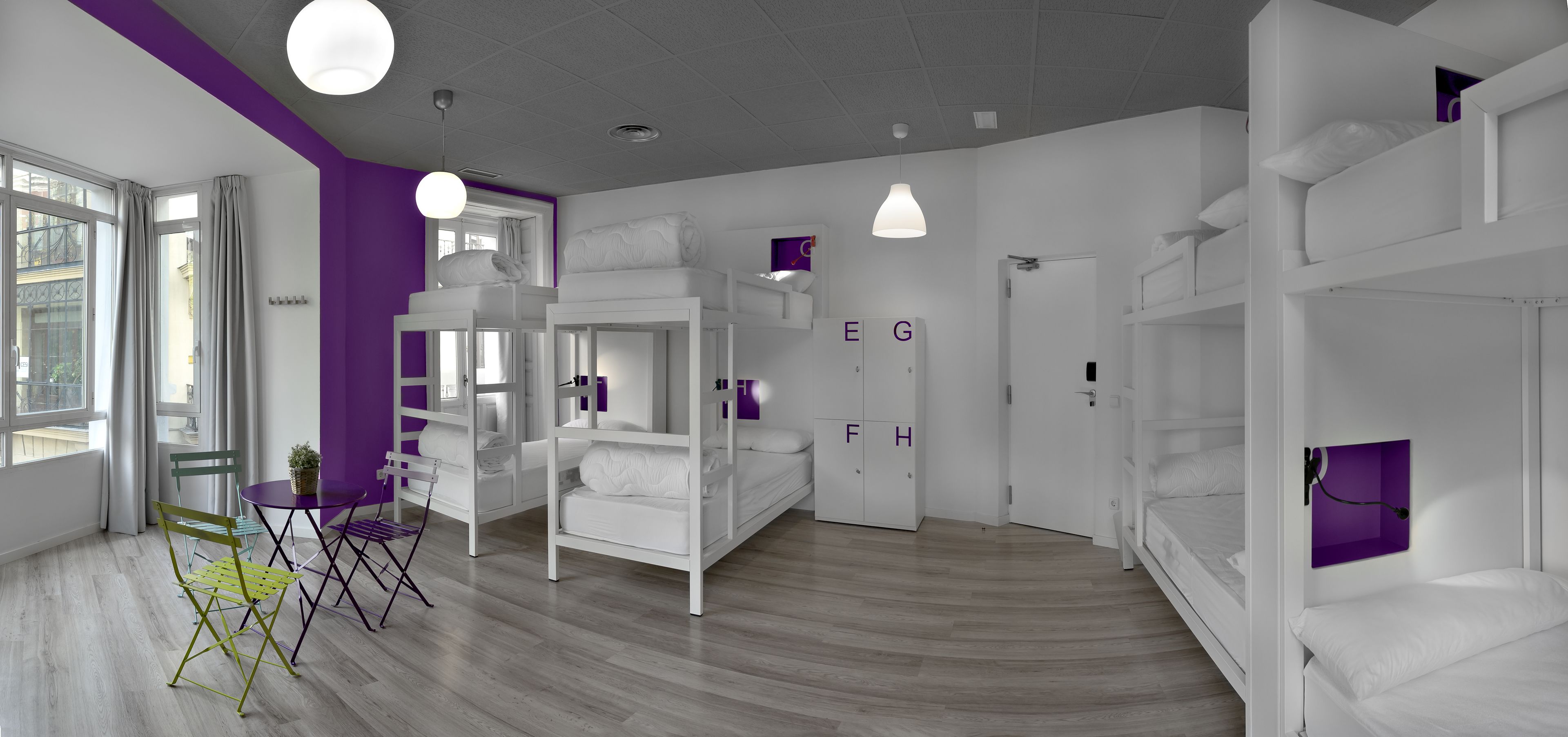Ein modernes Zimmer mit Etagenbetten, einem kleinen Tisch, Stühlen und einem fenster mit Vorhängen.