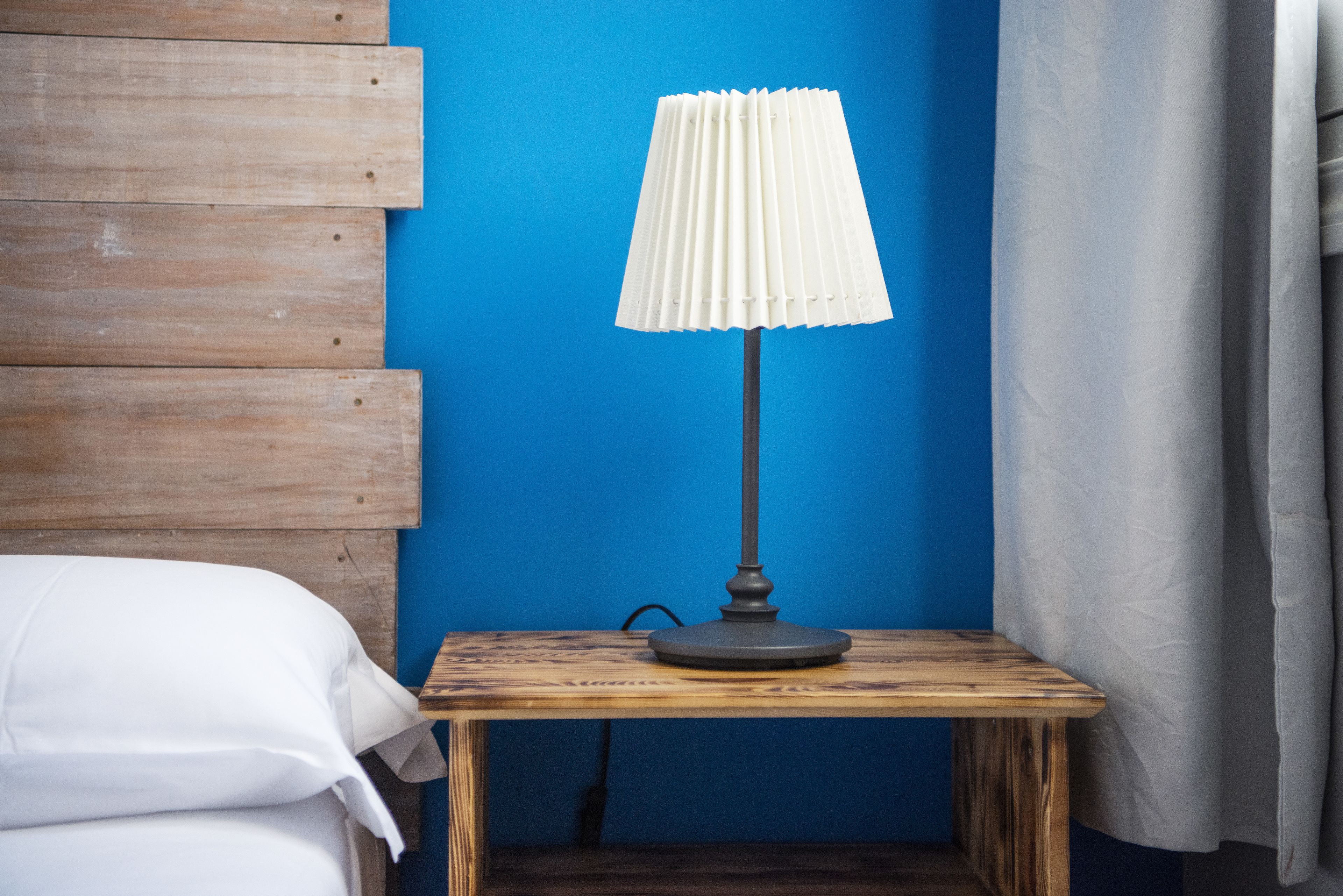 A wooden bedside table with a white lamp against a blue wall.