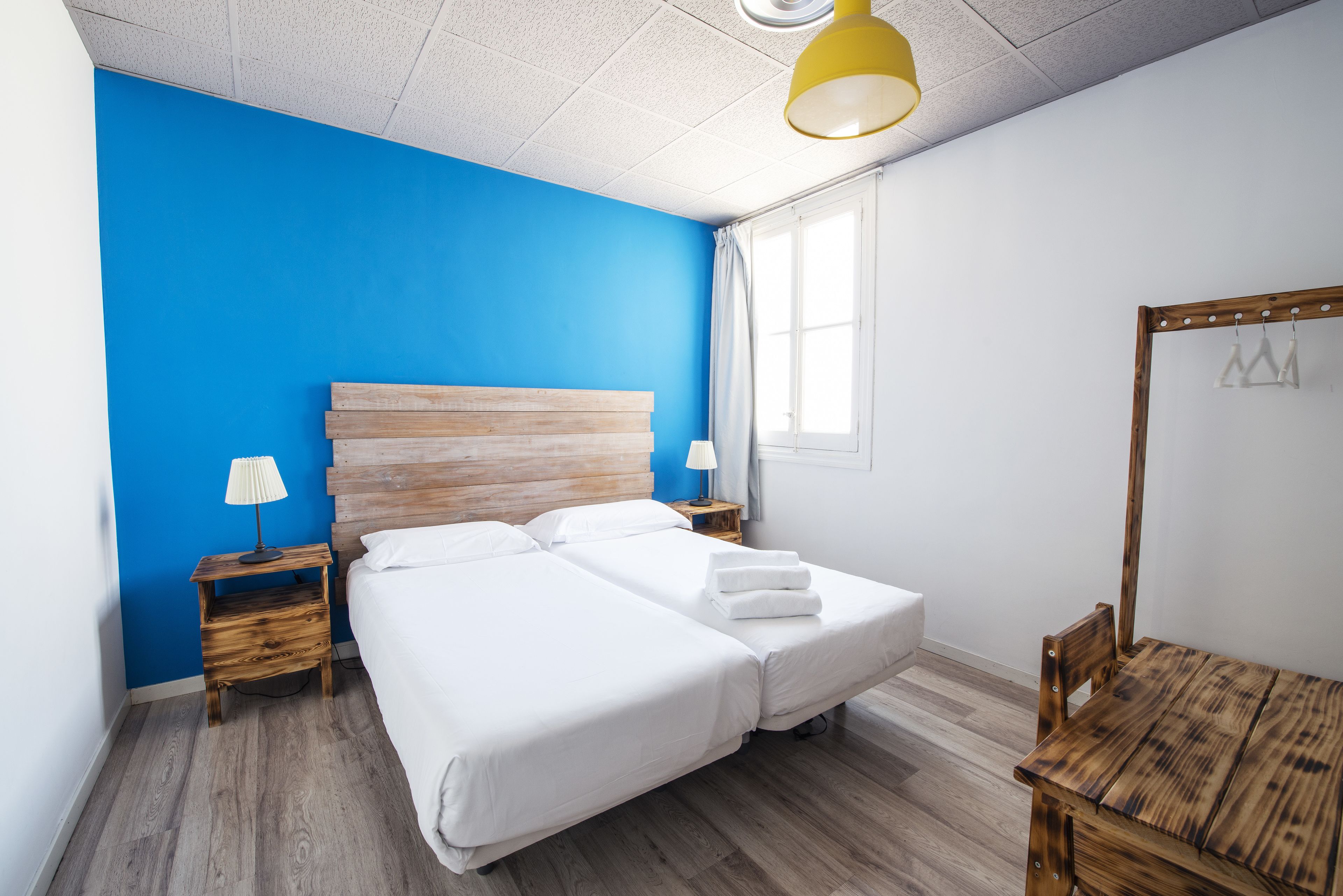 Una cama doble con ropa de cama blanca, un cabecero de madera, una mesita de noche con lámpara y una silla de madera.