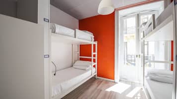 Een slaapzaal met stapelbedden, een witte garderobe en een feloranje accentmuur.