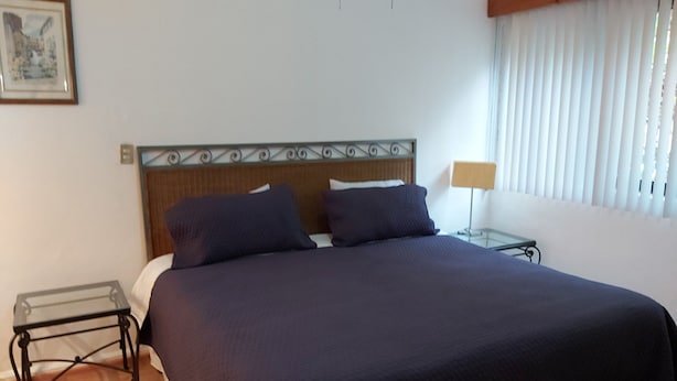 A neatly made bed with a dark blue bedspread and two pillows, a small bedside table with a lamp, and a framed picture on the wall. - Steinhaus Homero (Mexico City)