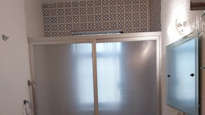 A bathroom with a shower enclosure, a sink with a mirror, and patterned tiles on the walls. - Steinhaus Homero (Mexico City)
