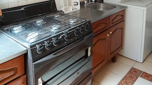 A kitchen with a gas stove, oven, wooden cabinets, white tiles, and a white refrigerator. - Steinhaus Homero (Mexico City)
