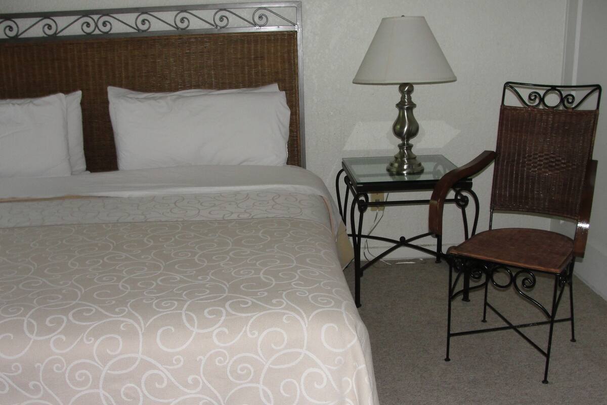 A hotel room with a large bed, a bedside table with a lamp, and a chair.