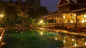 A pool area with a reflection of a traditional building, surrounded by greenery and lounge chairs. - Rajabori Villas (Kratie)