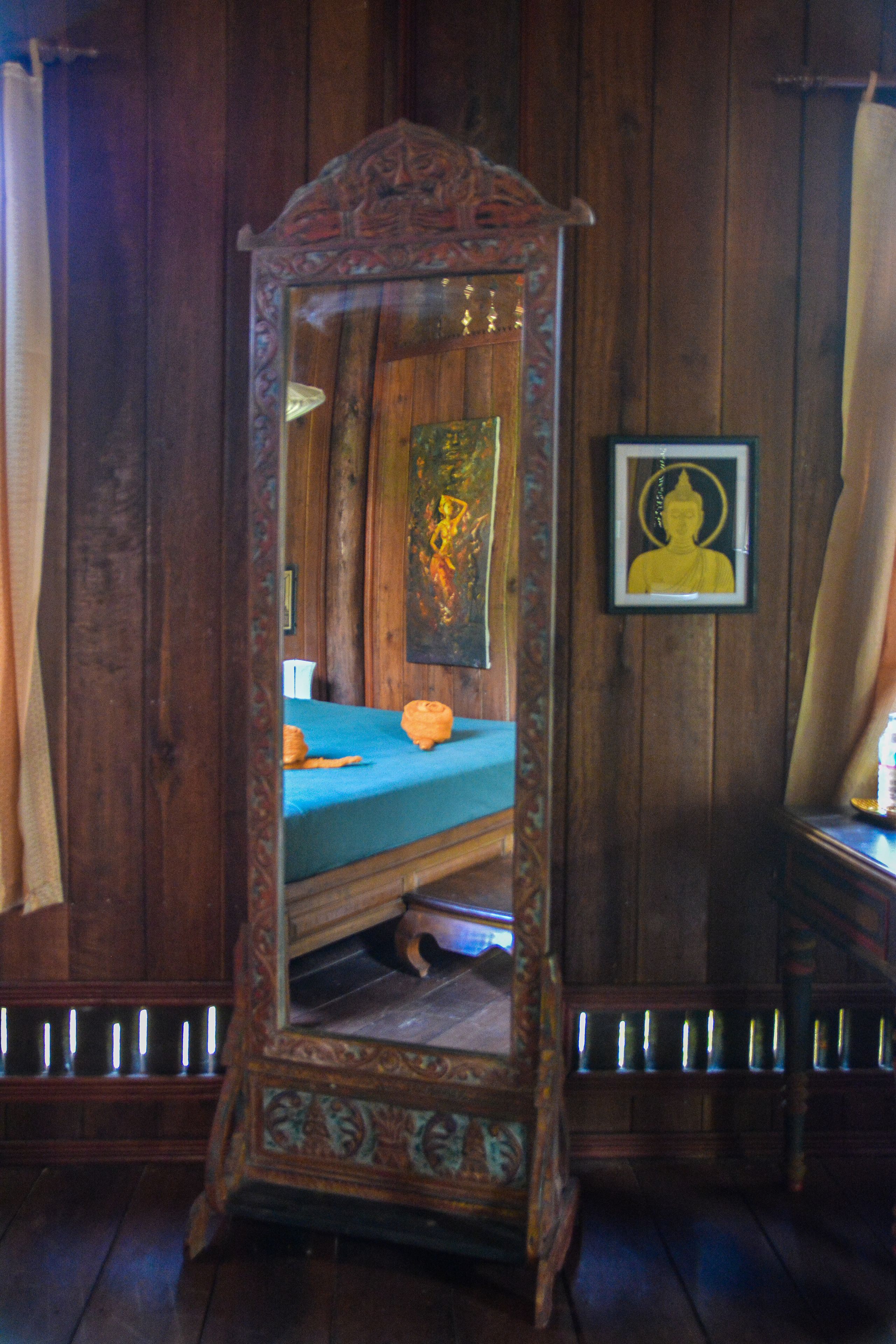 A wooden-framed mirror with a blue bedspread and a Buddha painting on the wall.
