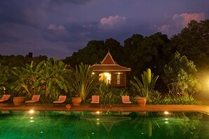 A pool area with lounge chairs and a building with a traditional roof in the background.