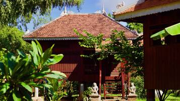 A traditional wooden building with a tiled roof, surrounded by lush greenery and stone statues.