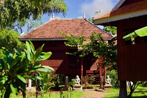 A traditional wooden building with a tiled roof, surrounded by lush greenery and stone statues.