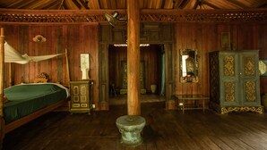 A room with wooden walls and ceiling, a bed with a canopy, a wooden stool, a mirror, and a cabinet. - Rajabori Villas (Kratie)