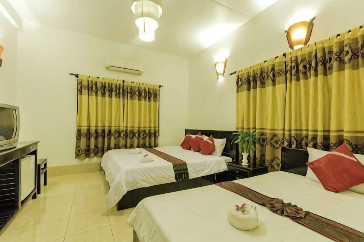 Habitación de hotel con dos camas, un escritorio, una silla, televisor, cortinas e iluminación en la pared.