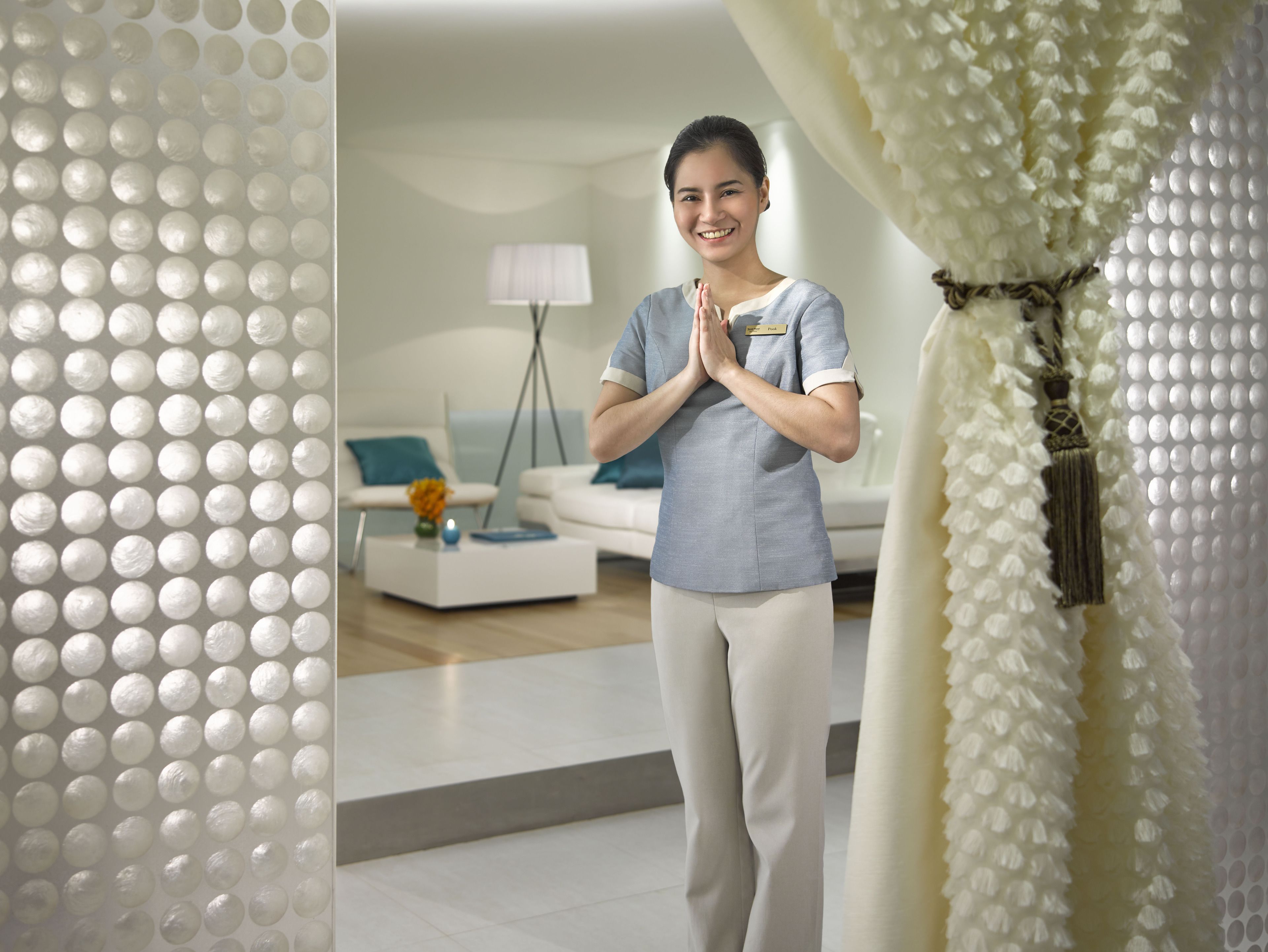 A person standing in a modern room with a white sofa, a lamp, and a decorative wall.