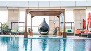 Una piscina con una pérgola de madera, sillas de descanso y un área de estar con forma de huevo.