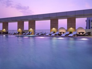 A rooftop pool area with lounge chairs and spherical seating pods, under a large overpass.