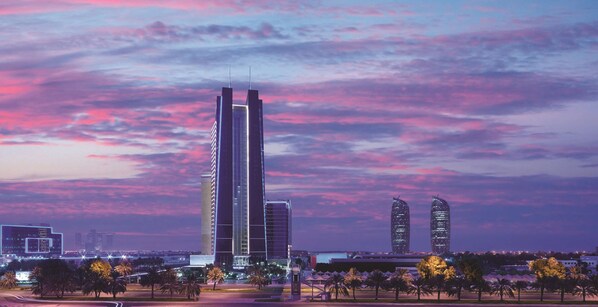 A cityscape with modern skyscrapers, a well-maintained park with palm trees, and a clear sky.