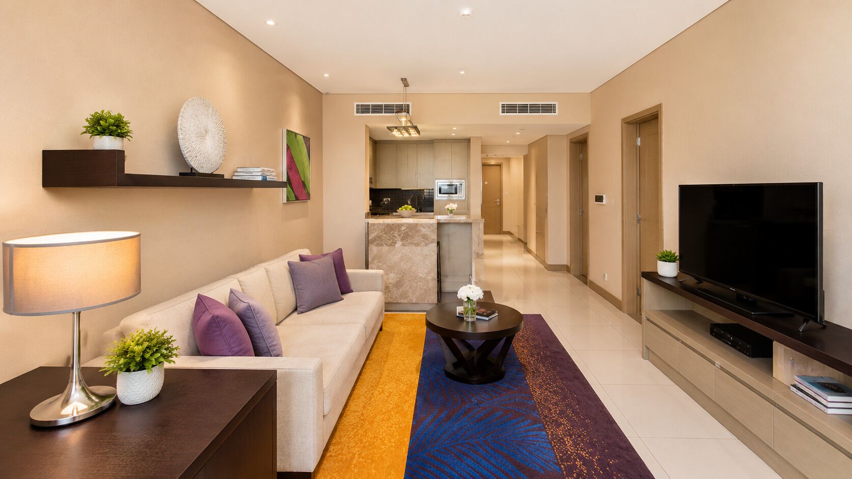 A modern living room with a sofa, a coffee table, a TV, and a kitchen in the background.