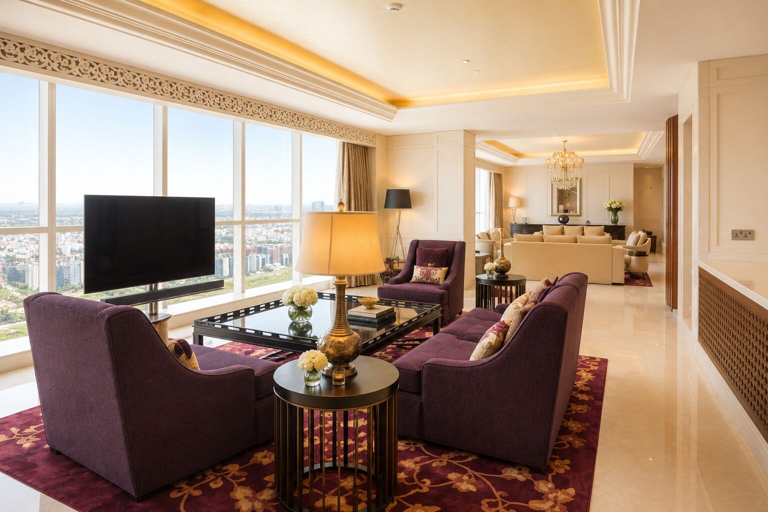A spacious living room with a large flat-screen TV, comfortable seating, a chandelier, and a view of the city.