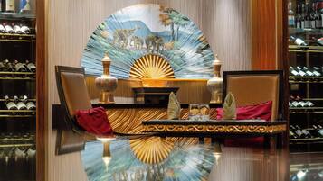 Une chambre luxueuse avec un mur recouvert de miroirs, une table ronde agrémentée d’un élément décoratif central et un meuble à bouteilles de vin.