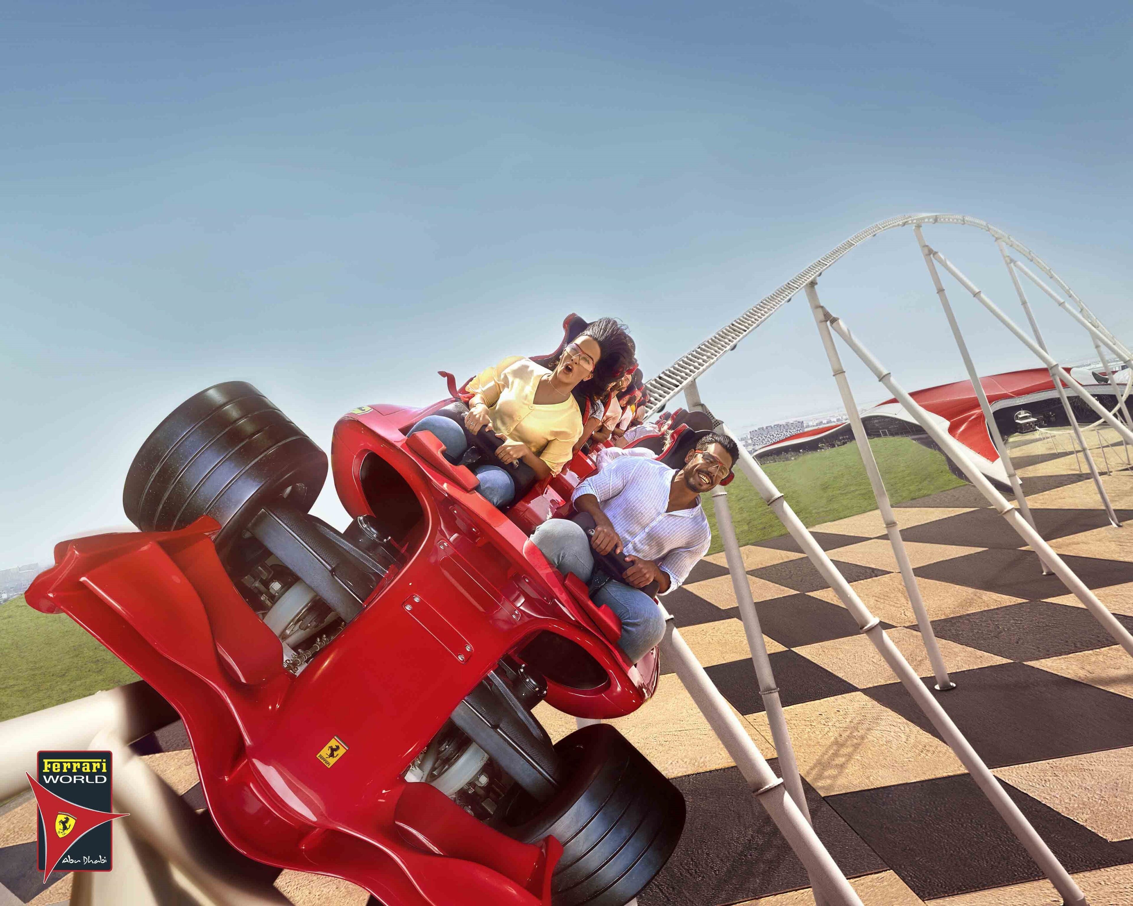 Une grande roue dont le plancher présente un motif à carreaux et dans laquelle une voiture rouge est en mouvement.
