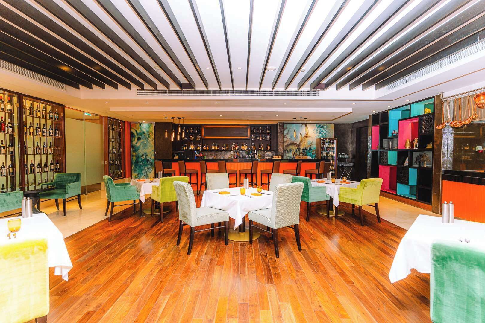 Ein Restaurant mit Holzboden, grün-weißen Stühlen und einer Bar mit Regalen voller Flaschen.