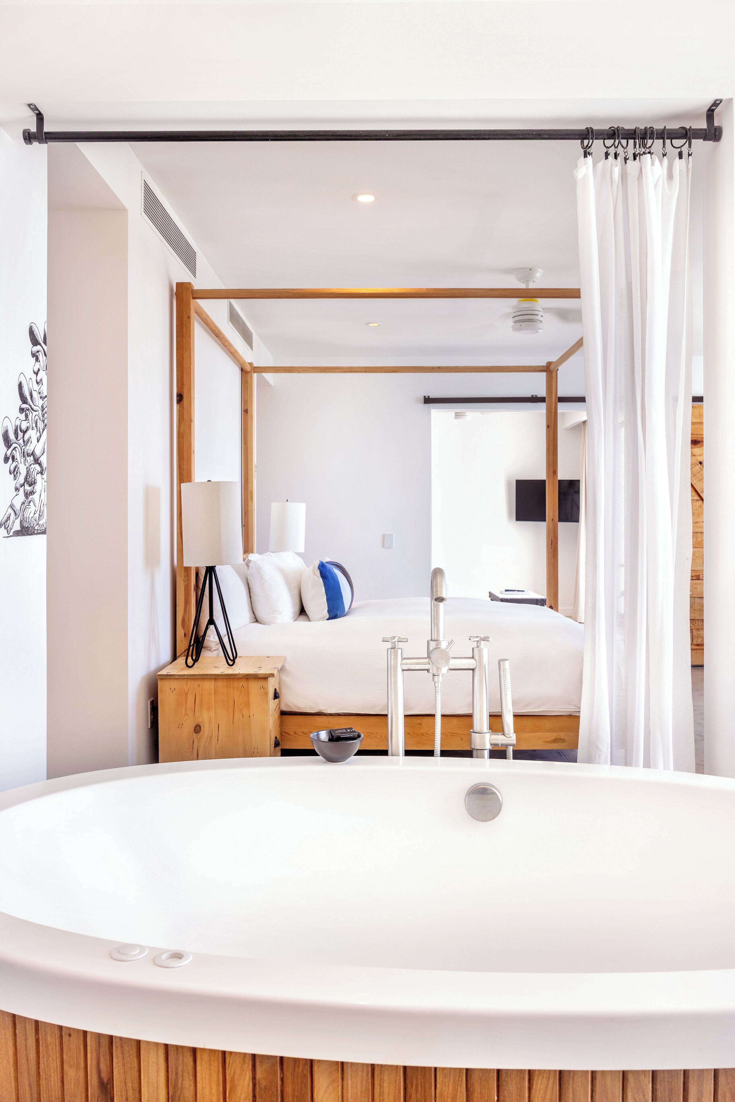 Een moderne slaapkamer met een groot ligbad, een houten nachtkastje, een bed met wit beddengoed en een televisie aan de muur.