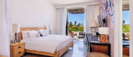 A modern hotel room with a wooden bed, a desk, and a balcony with a view of palm trees.