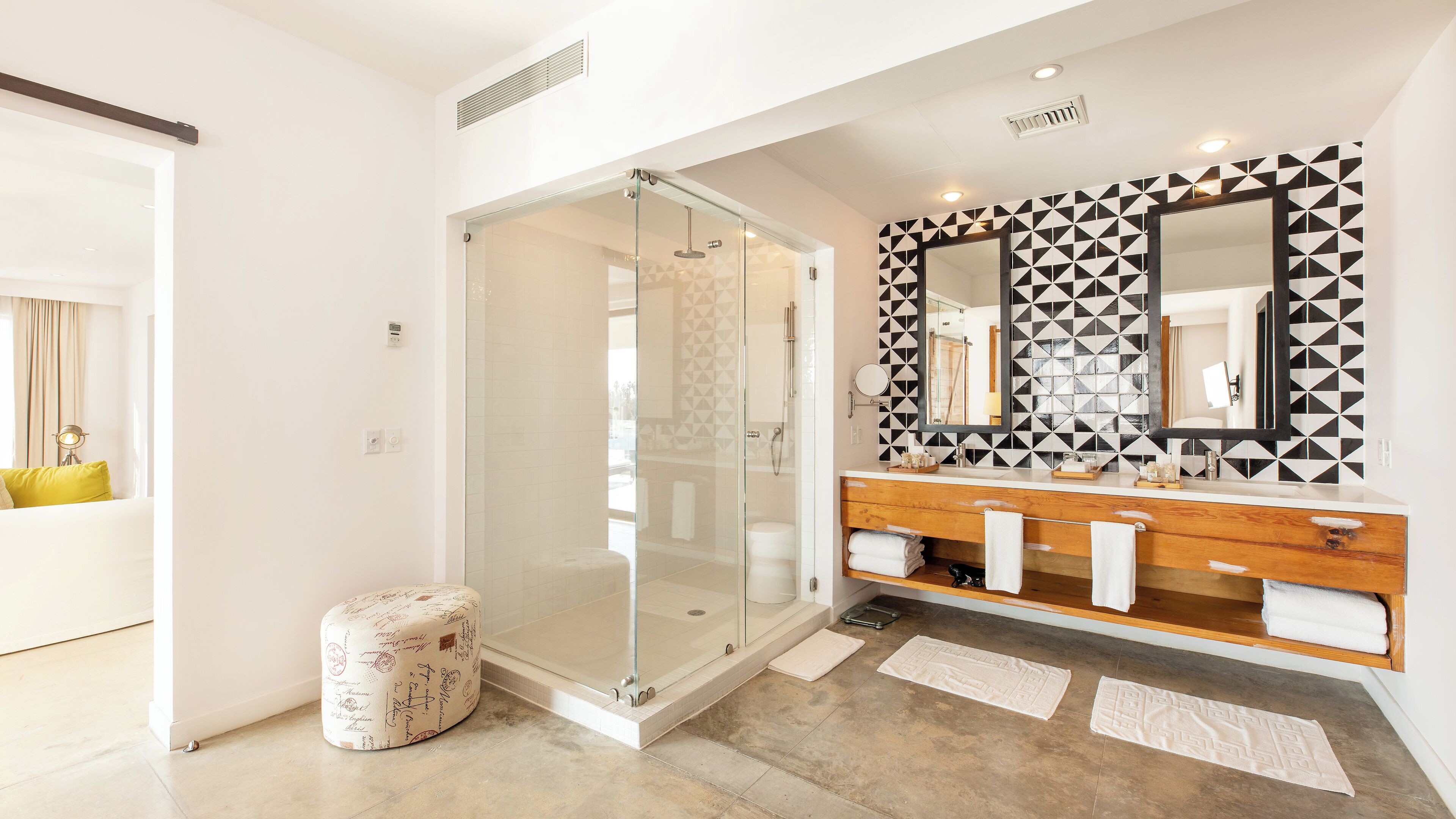 A modern bathroom with a glass-enclosed shower, a wooden vanity with a mirror, and a geometric-patterned wall.