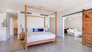 A modern bedroom with a four-poster bed, a wooden wardrobe, and a white sofa in the adjacent room.