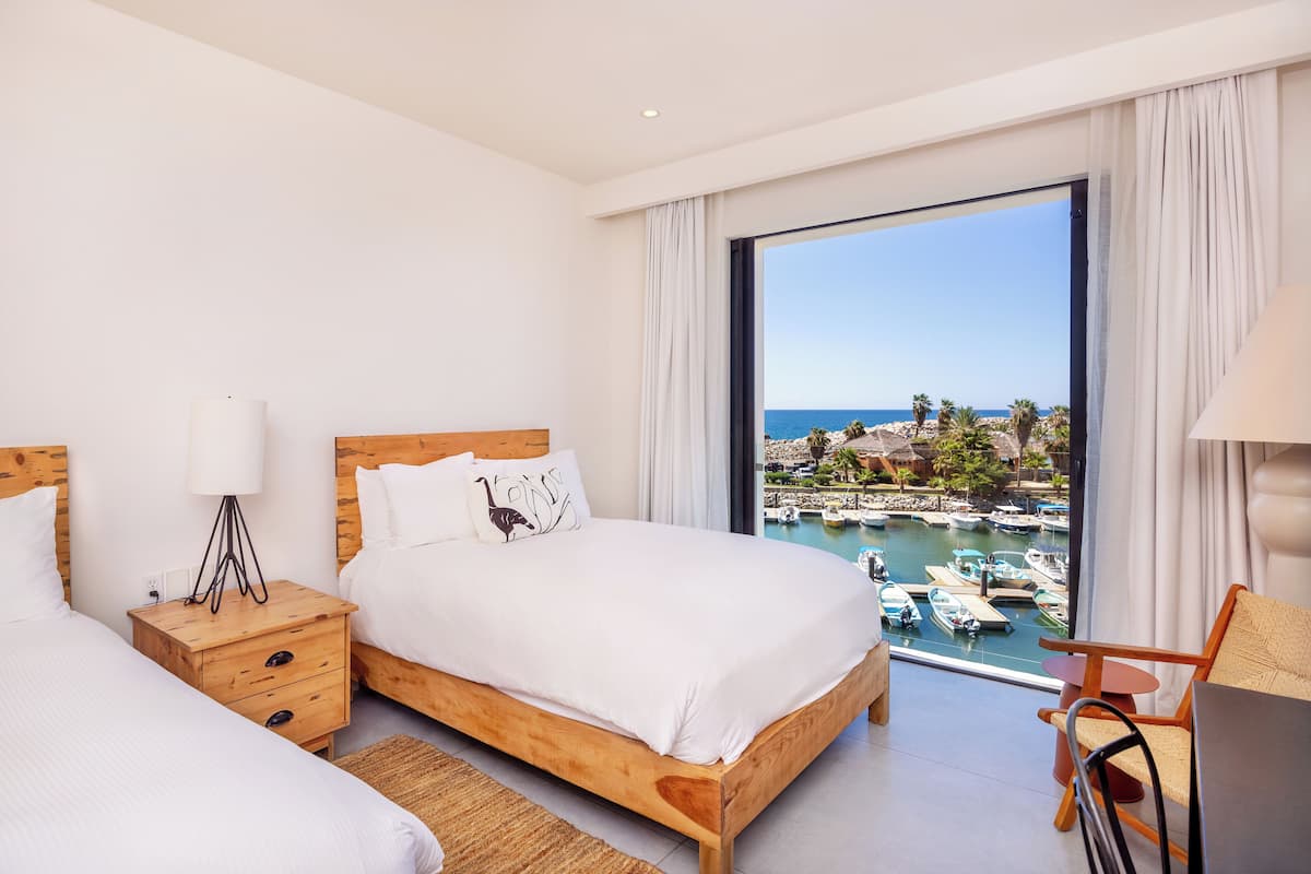 A hotel room with a large window, wooden bed, bedside table, and a chair.